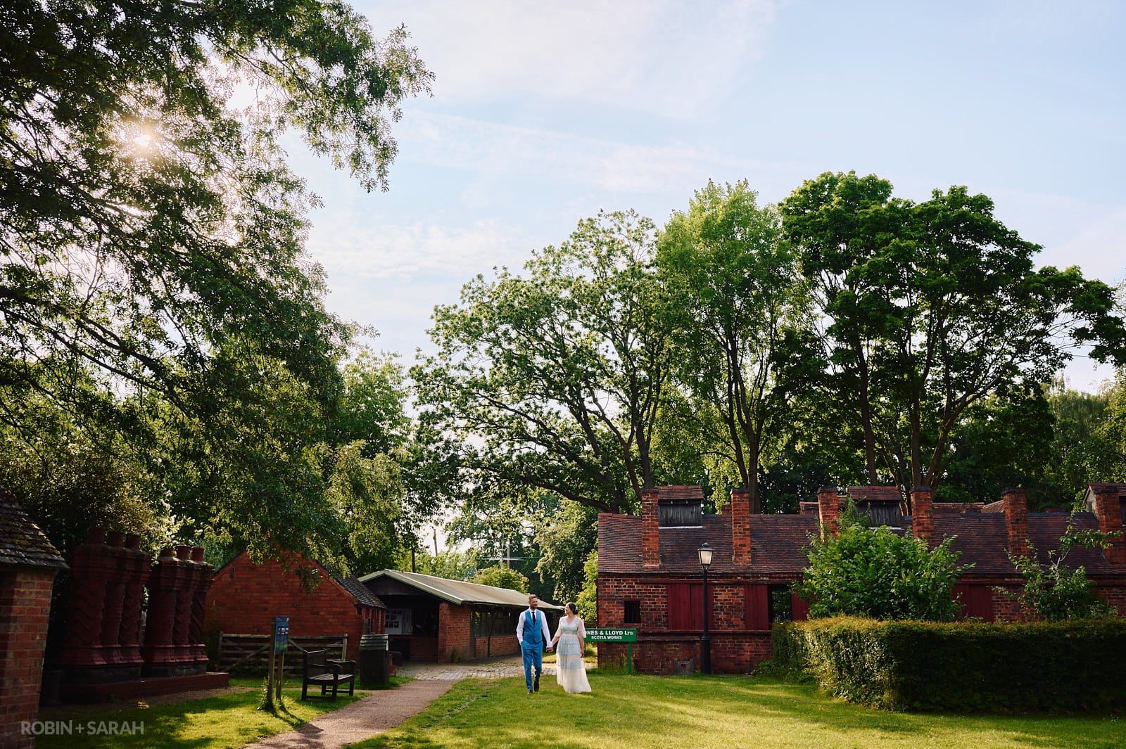 Bride and groom walk amongst old buildings at Avoncroft Museum on a beautiful summer evening.