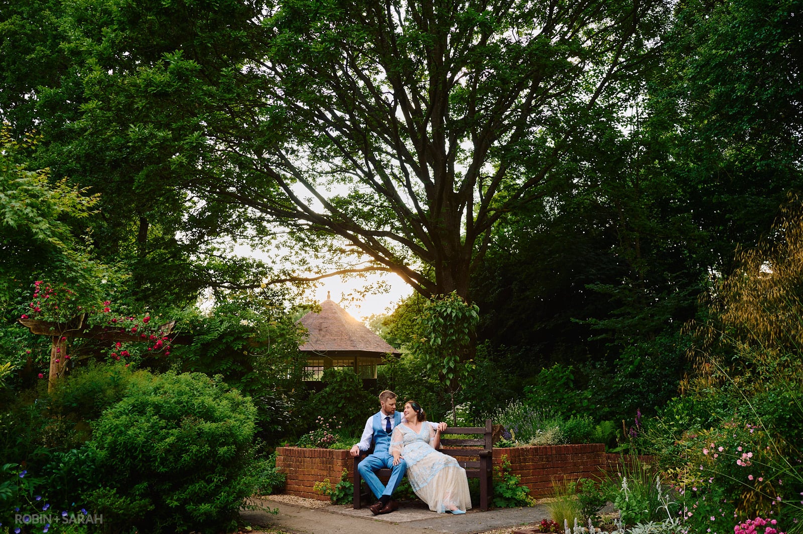 Bride and groom sitting together on bench surrounded by beautiful gardens at Avoncroft Museum