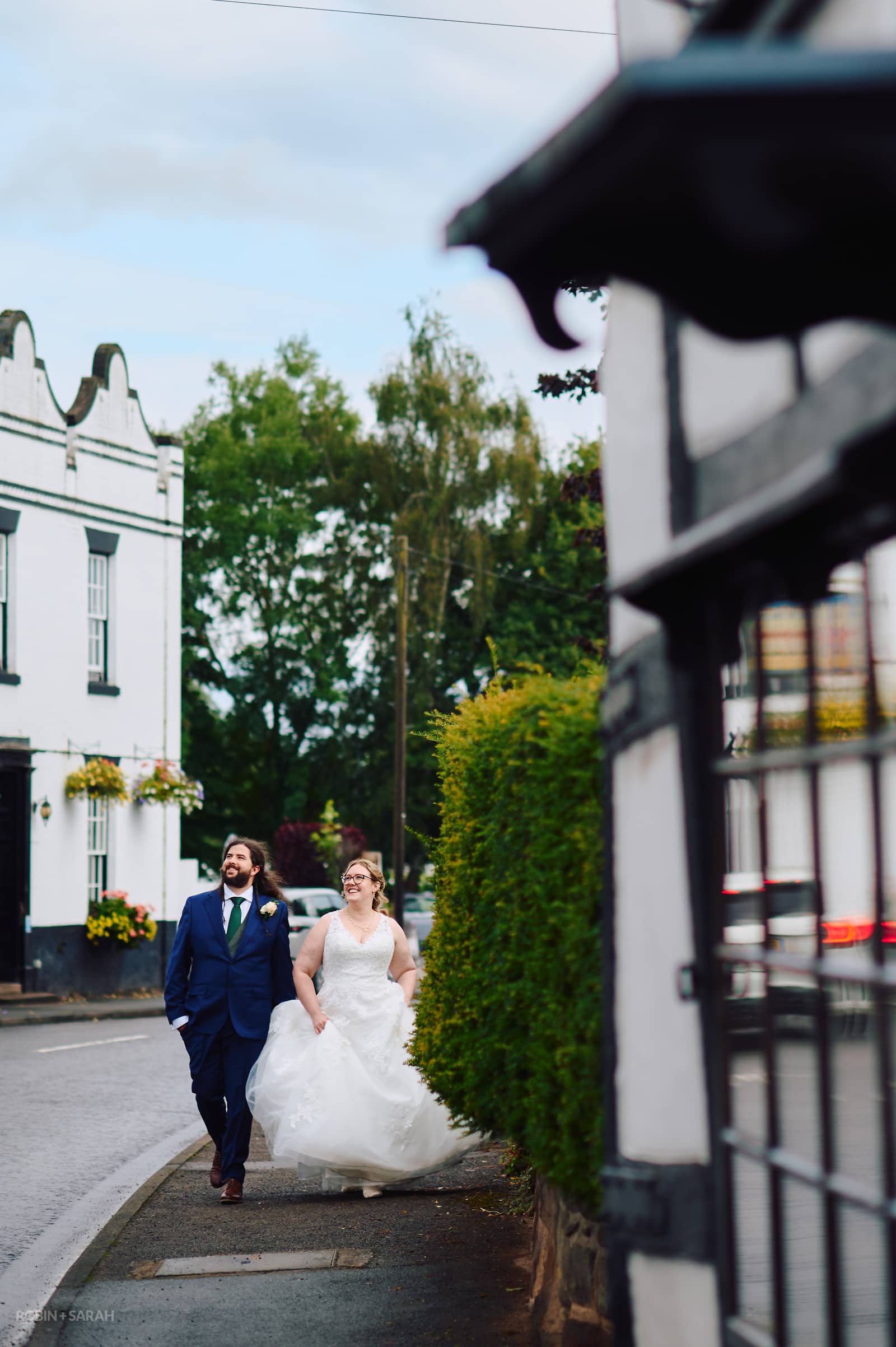 Bride and groom walk down high street in Ombersley with The Crown & Sandys pub in background