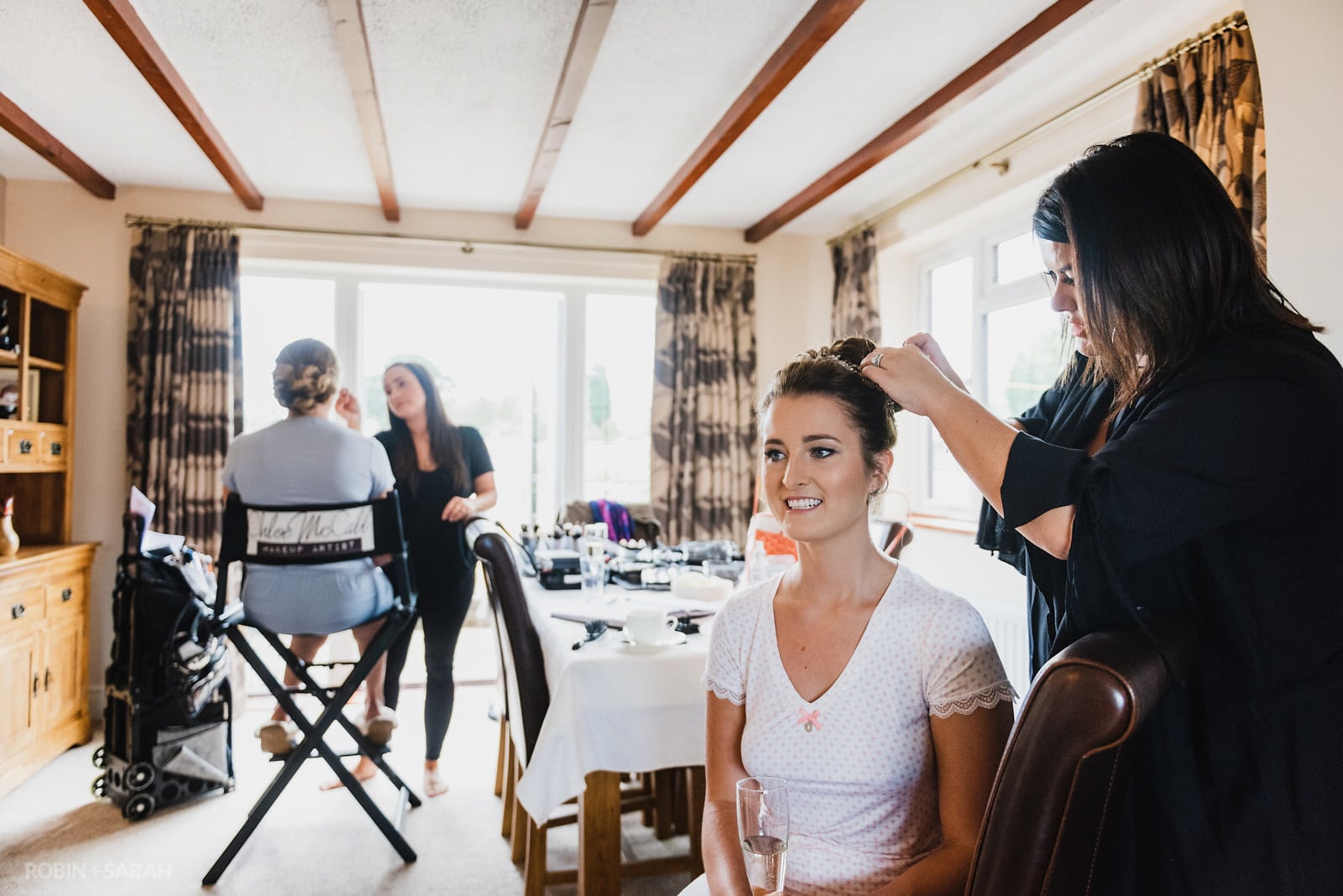 Bride has hair styled while bridesmaid has makeup applied