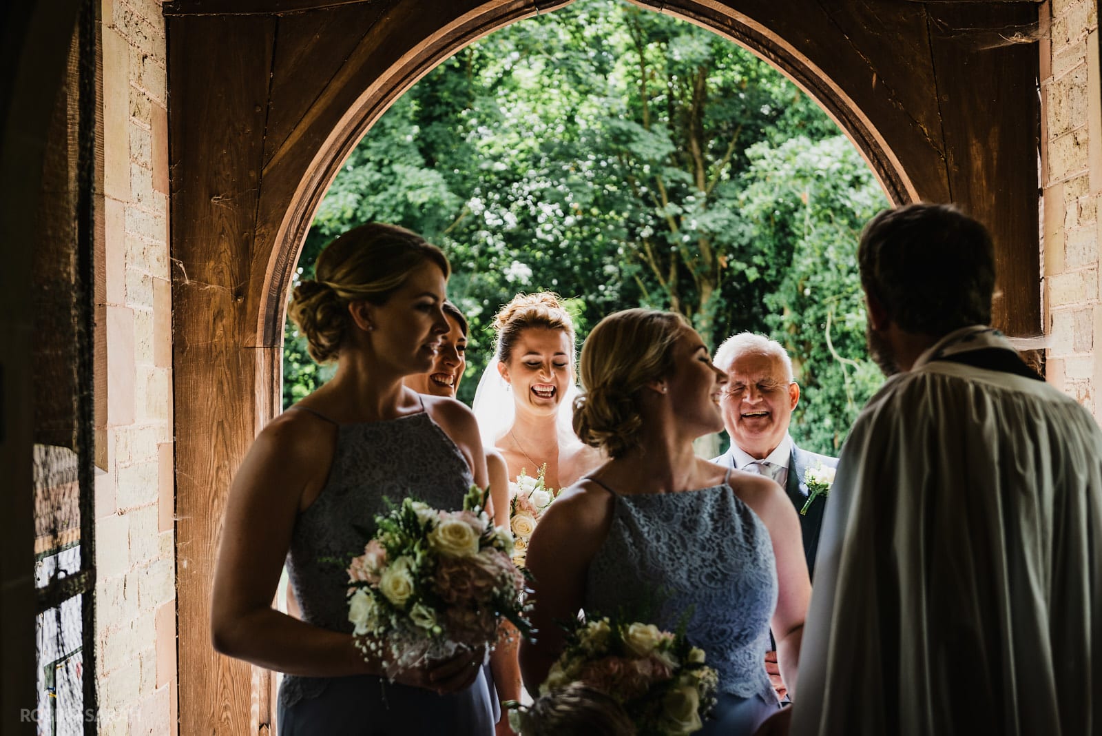 Bride, dad and bridesmaids laughing before they enter church for wedding ceremony