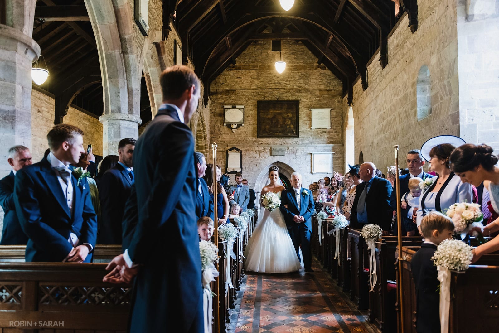 Bride and dad walk up aisle of St Peter's Church Diddlebury as groom waits
