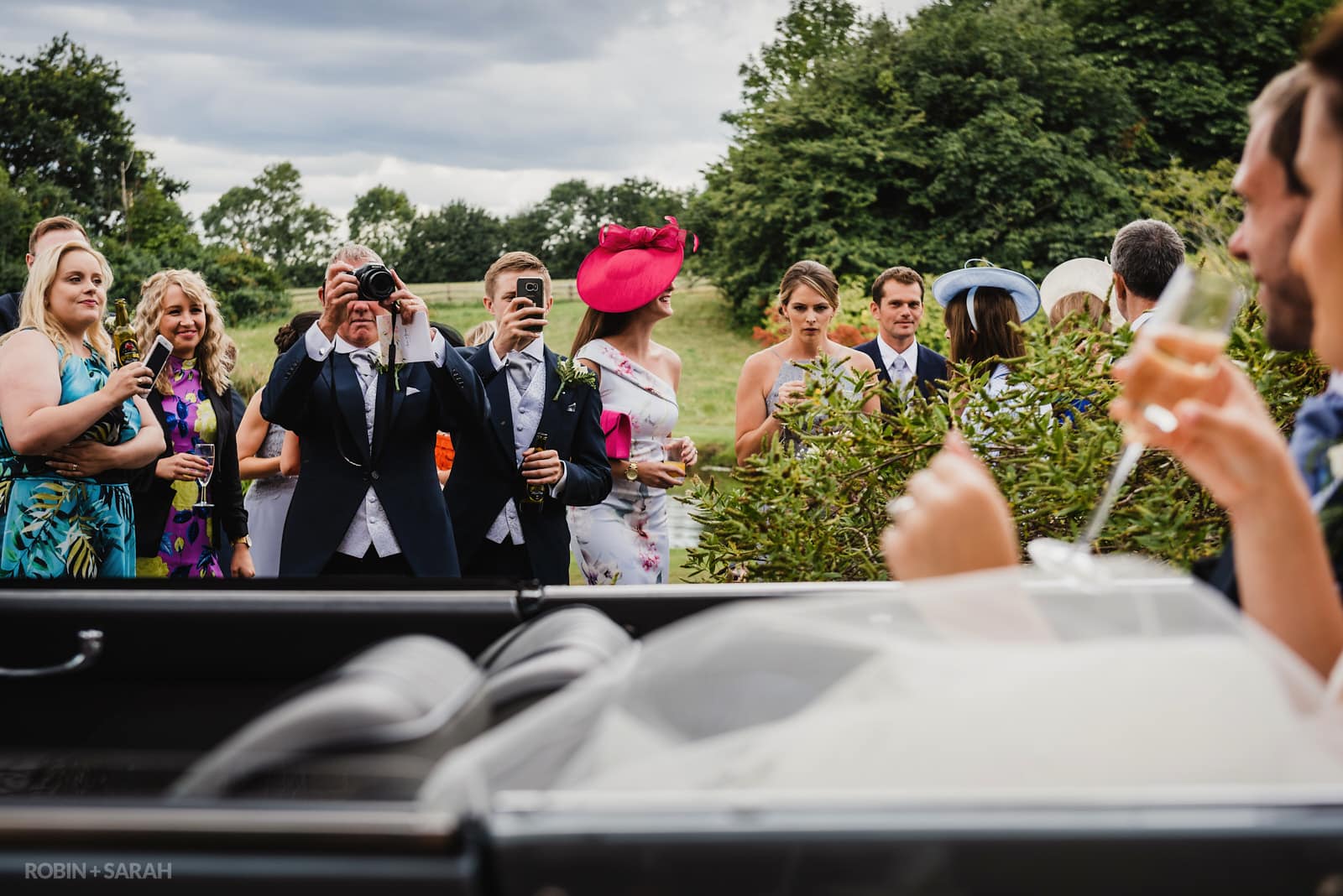 Wedding guests take photos of bride and groom in car