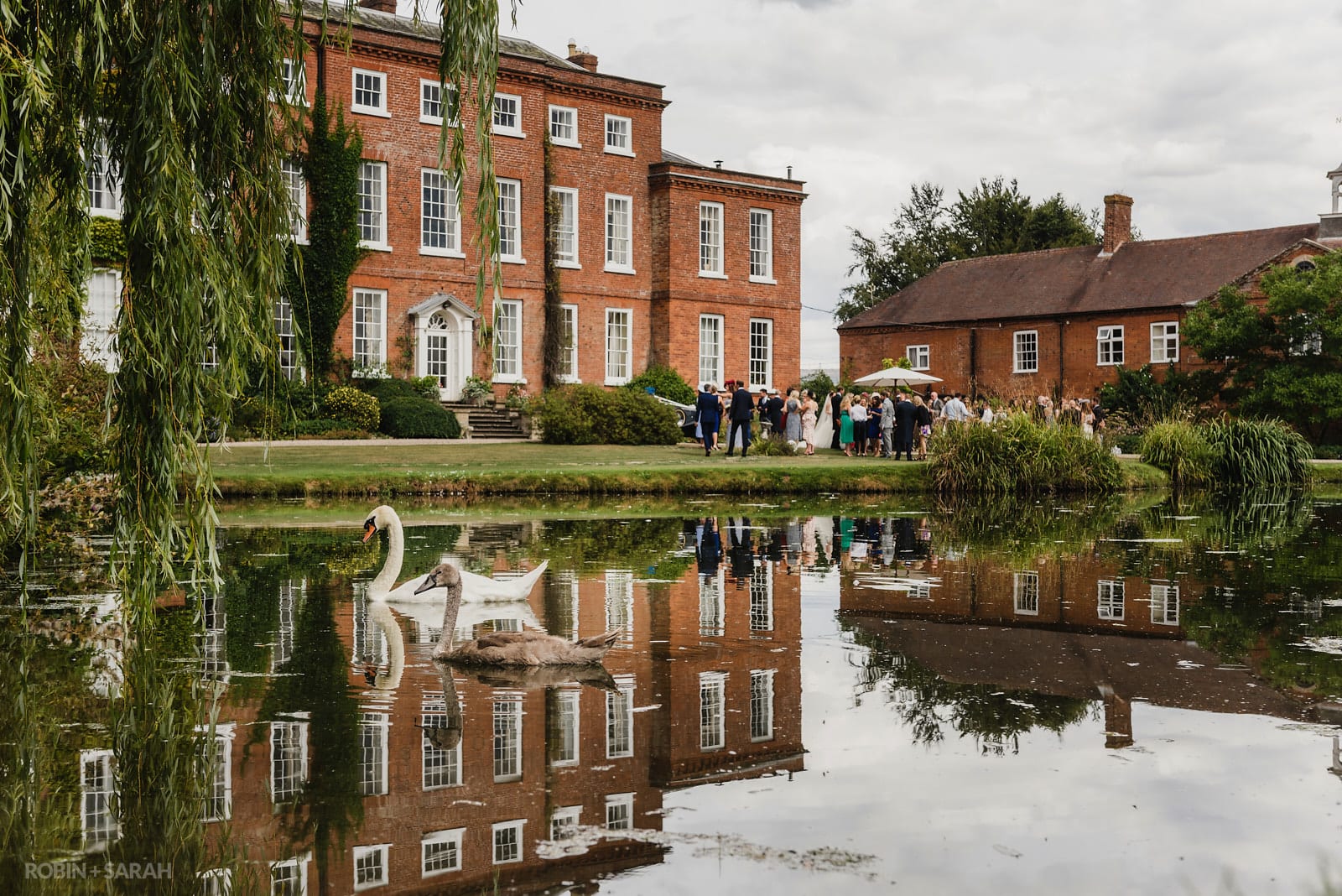 Guests drink and chat during wedding reception at Delbury Hall as two swans swim past on pond