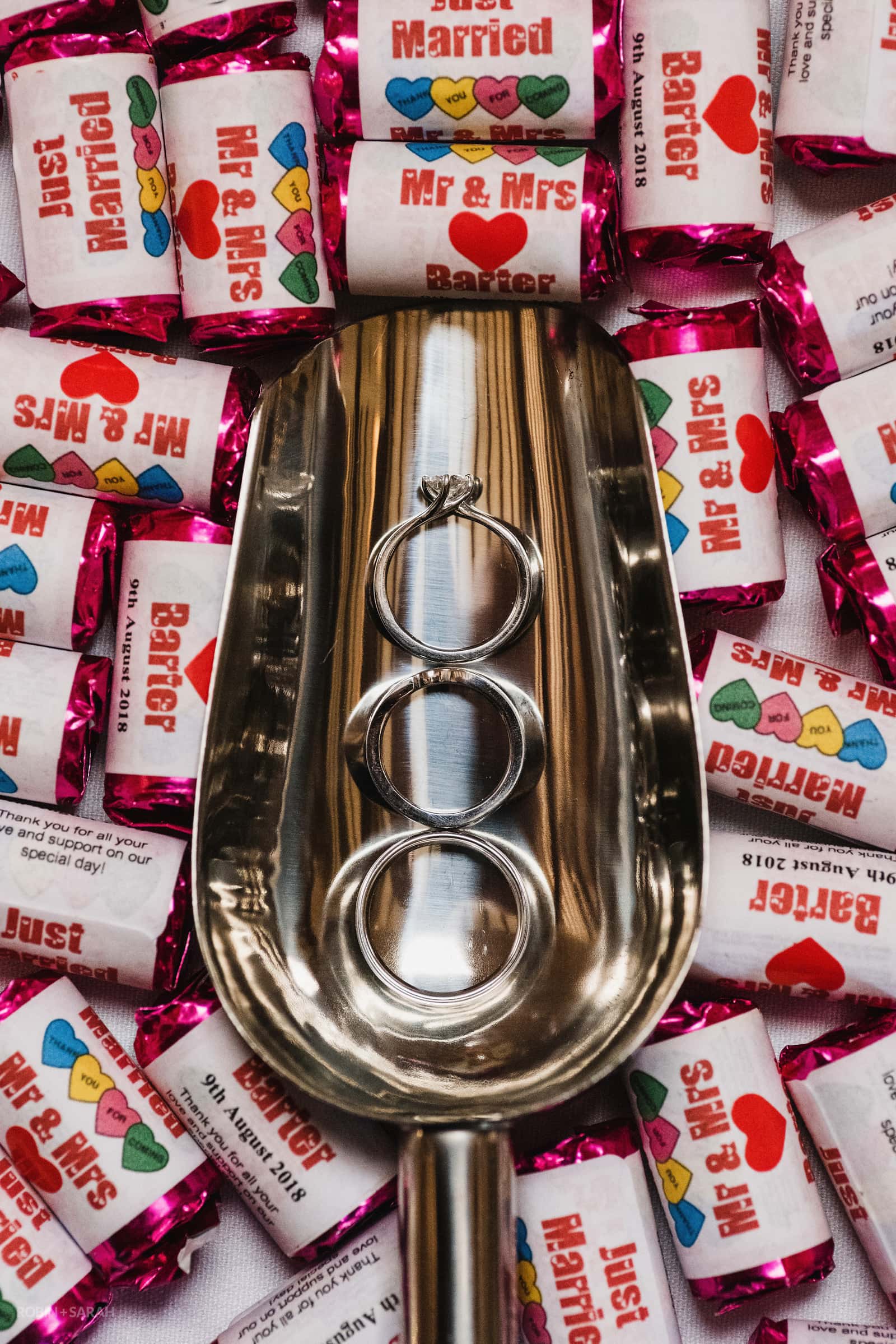 Detail of wedding and engagement rings in metal scoop surrounded by sweets