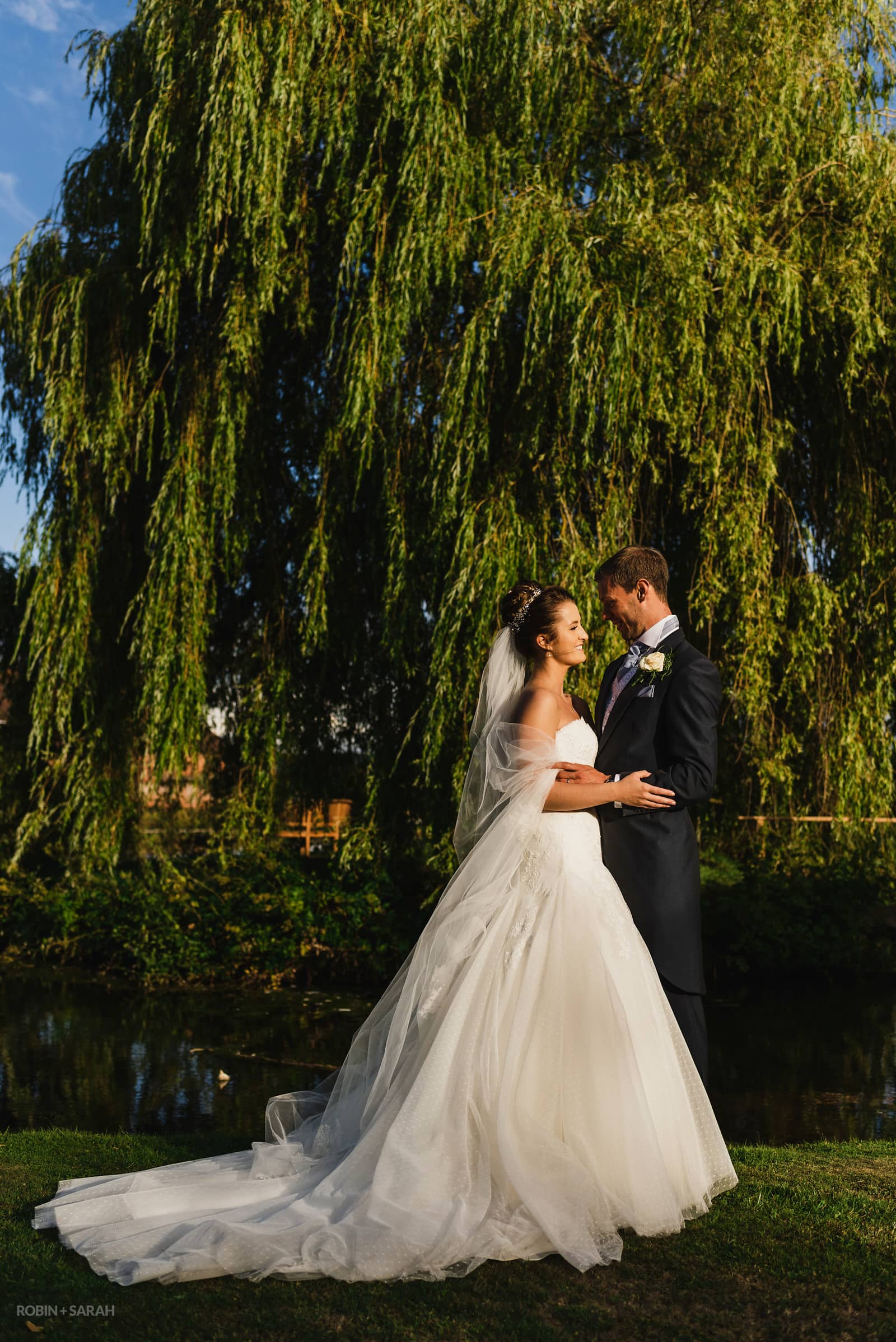 Bride and groom standing next to pond and trees in beautiful evening light