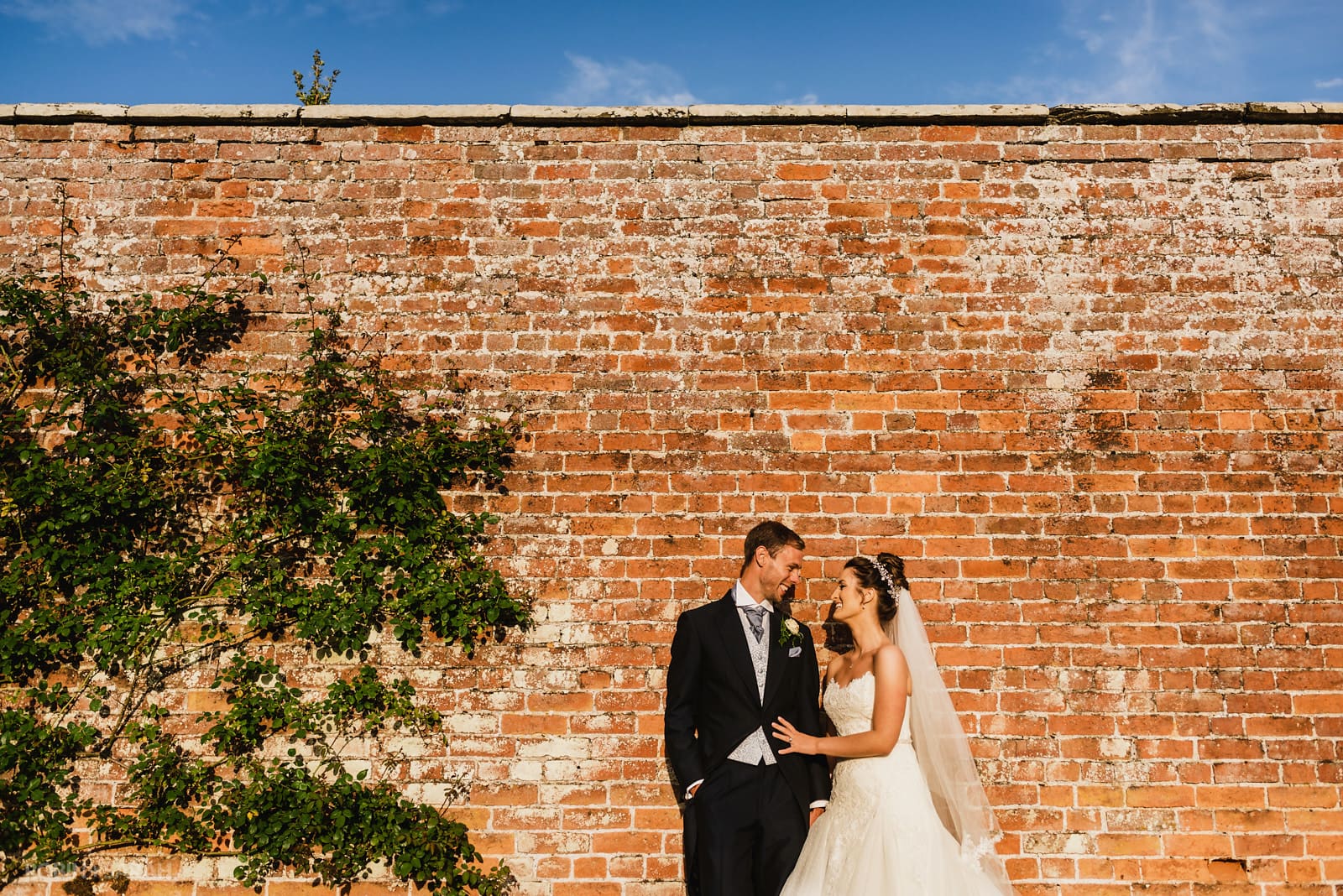 Bride and groom next to beautiful old brick wall in gardens at Delbury Hall