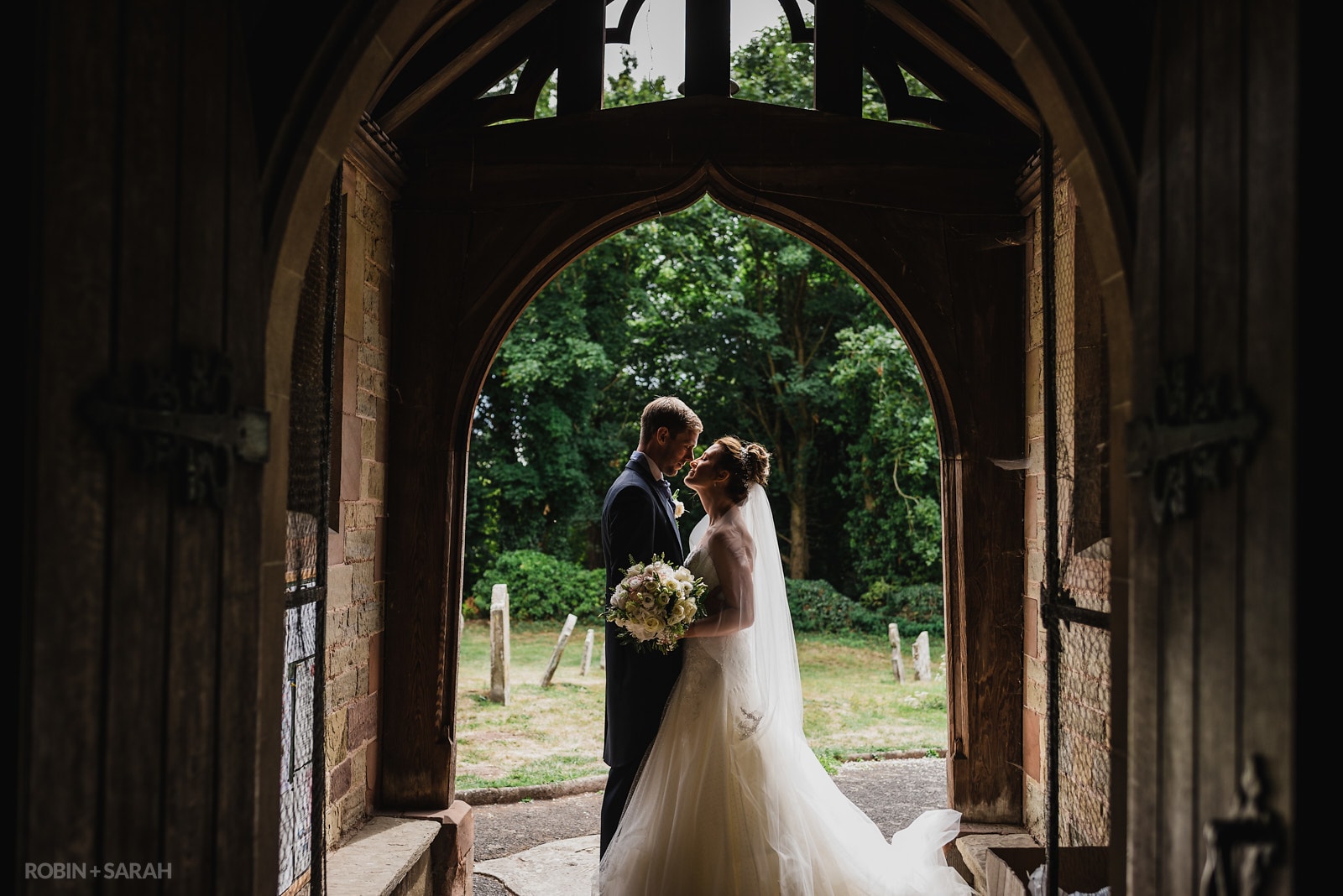Bride and groom about to kiss under arched doorway at St Peter's Church Diddlebury