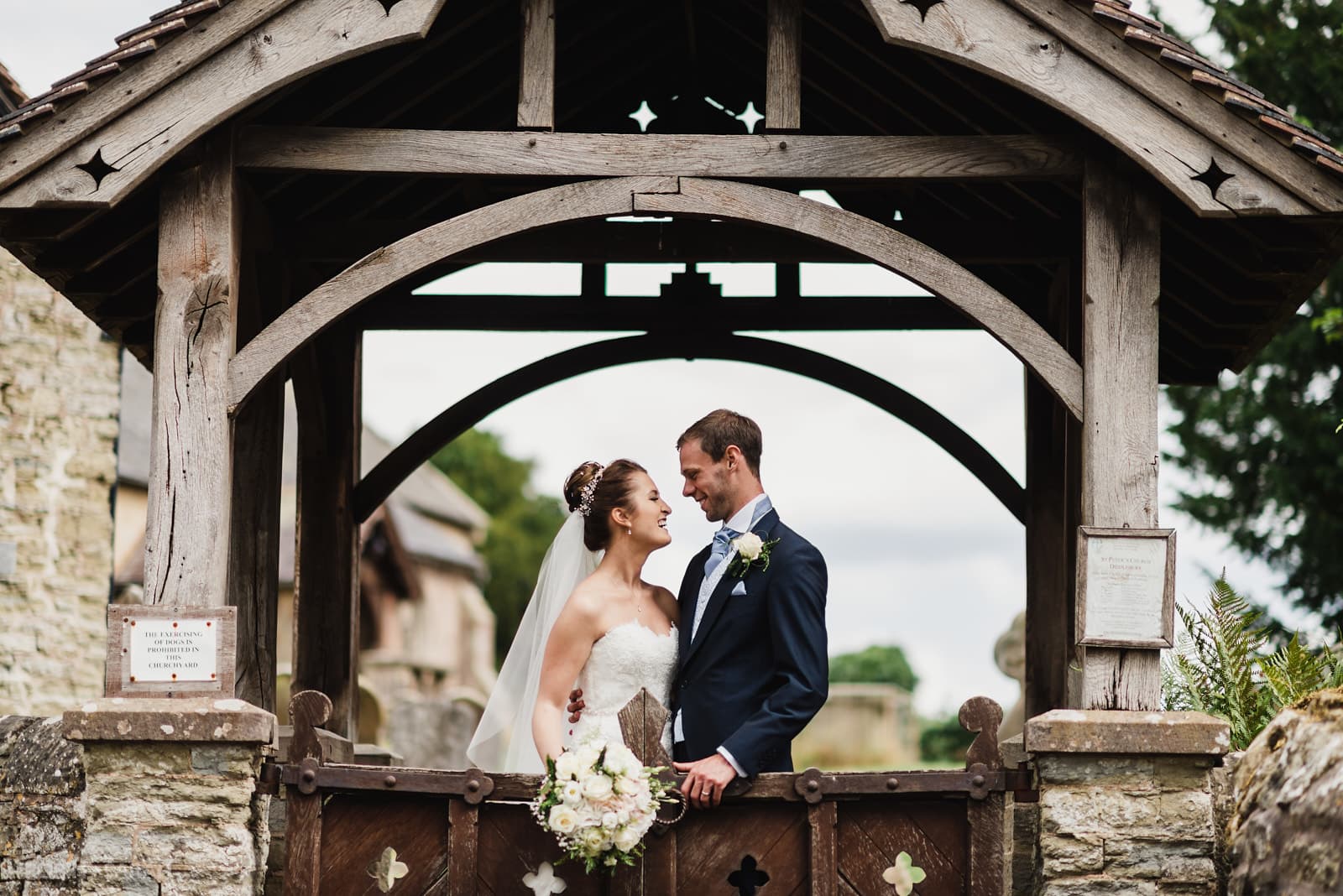Bride and groom under lychgate at St Peter's Church Diddlebury