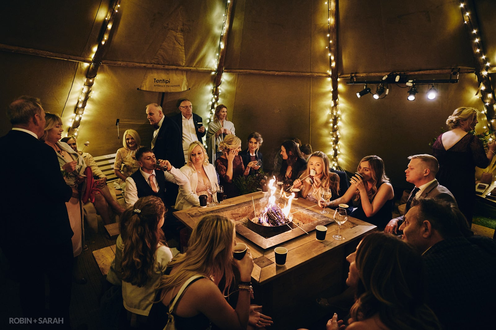 Wedding guests toast marshmallows on fire pit