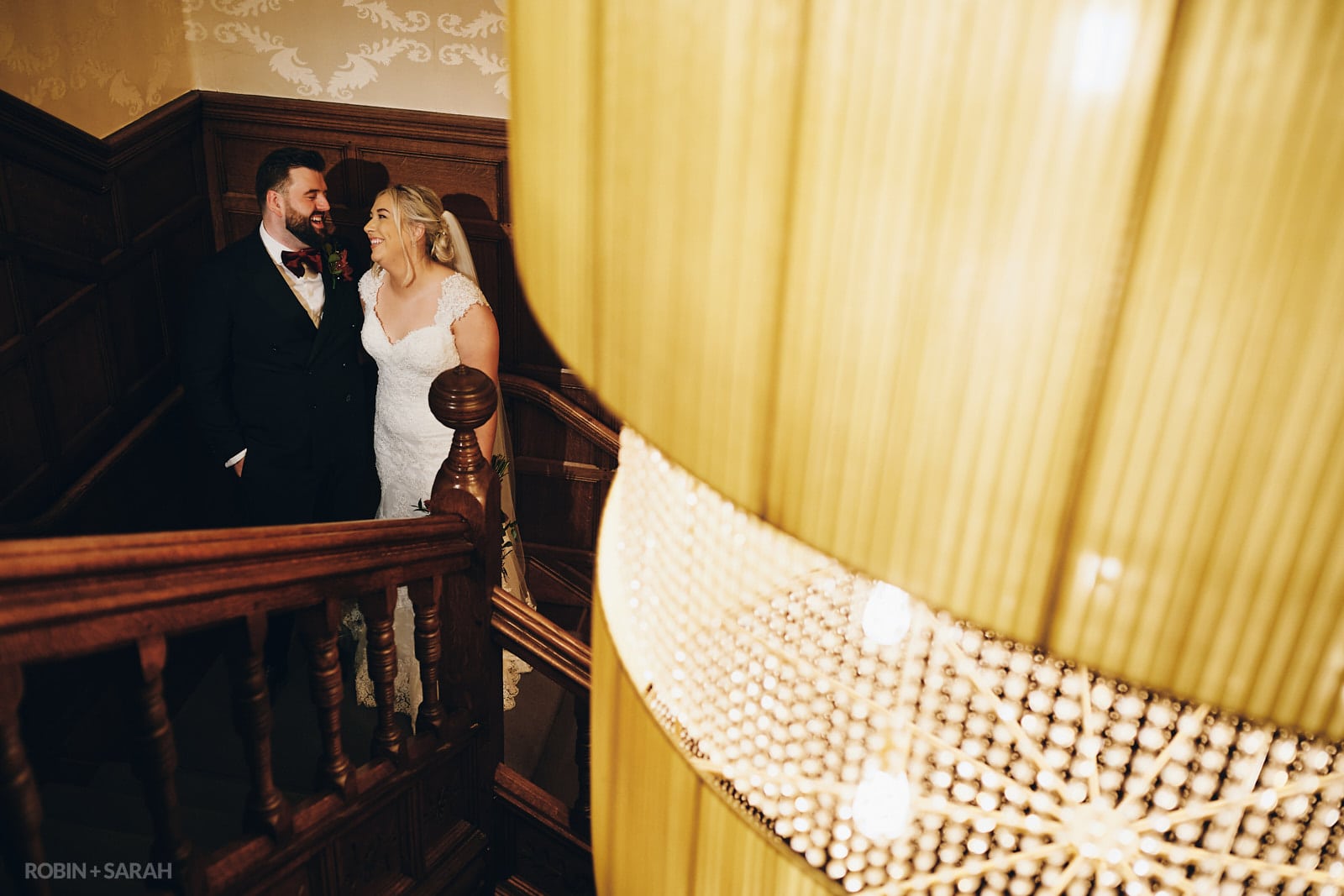 Bride and groom on staircase with enormous chandelier at Hampton Manor