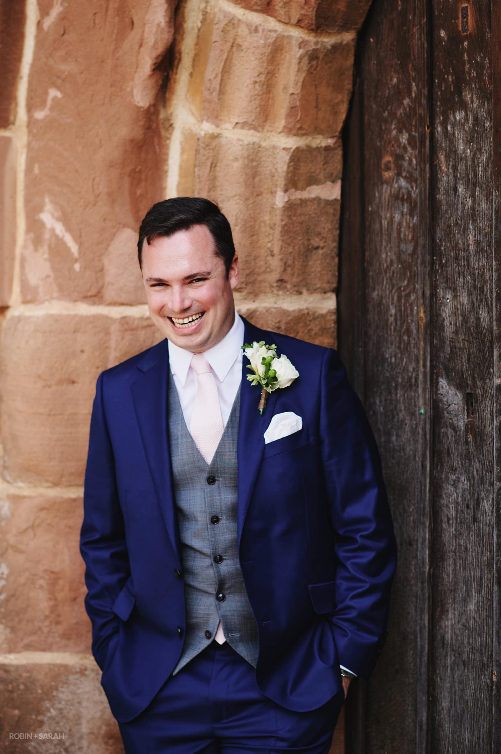 Portrait of groom laughing in doorway at Peter's church Dunchurch