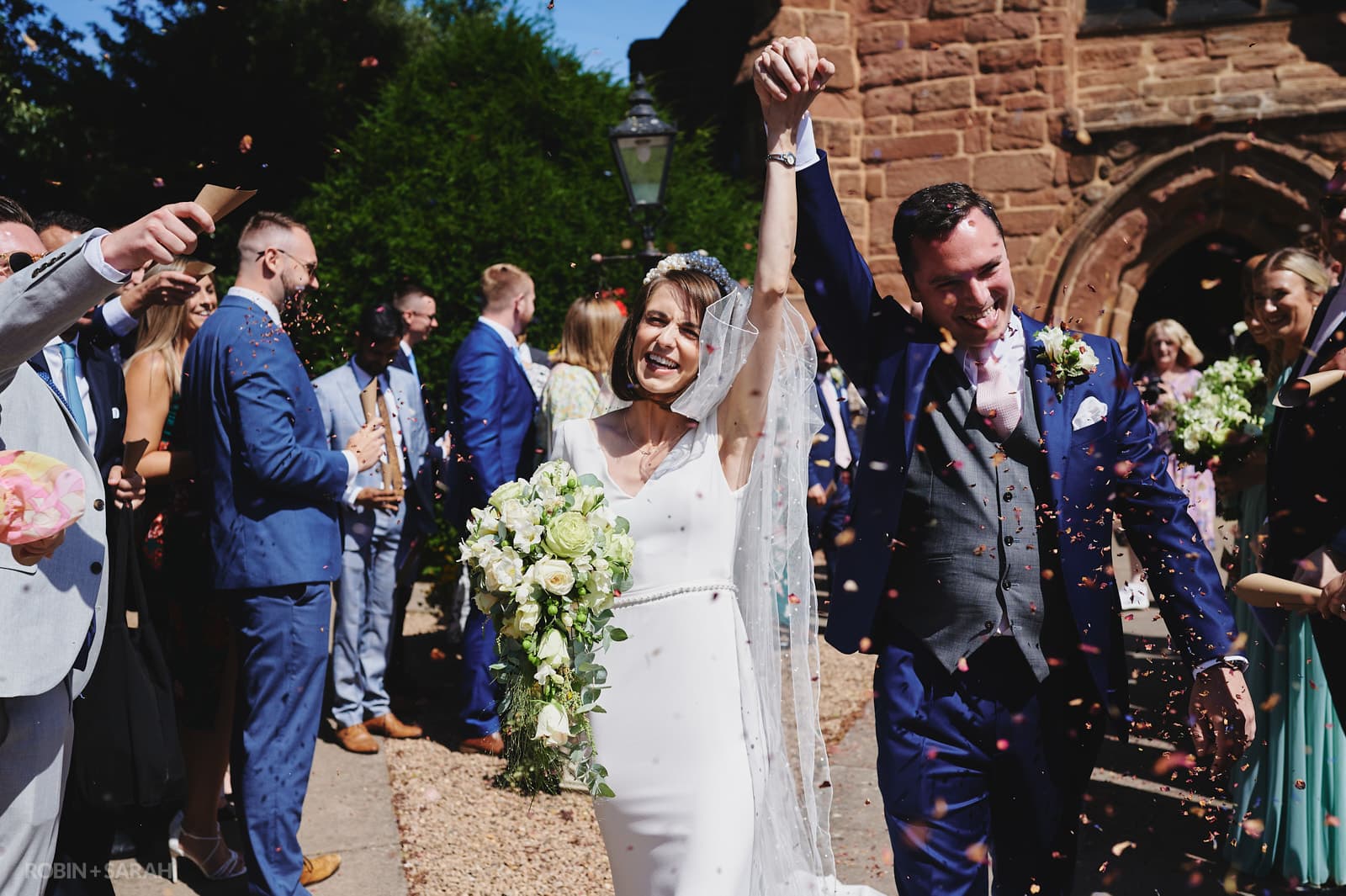 Bride and groom hold hands as they walk through confetti throw at St Peter's chuch Dunchurch