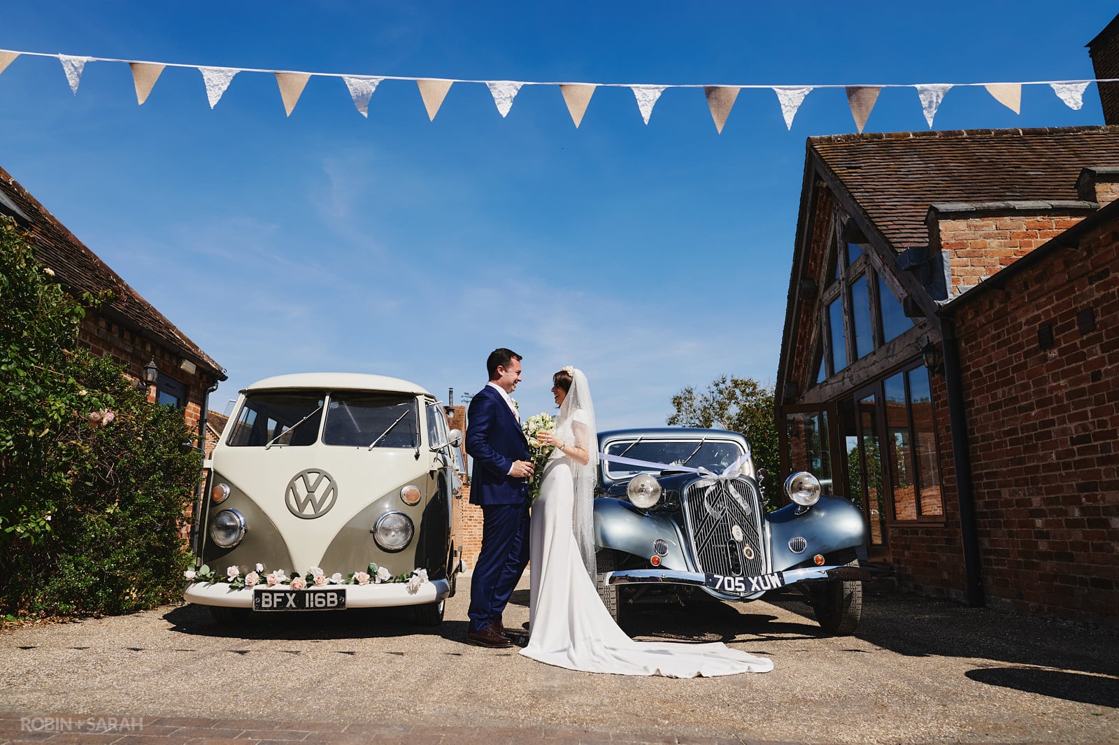 Bride and groom standing between wedding car and VW campervan at Wethele Manor in Warwickshire