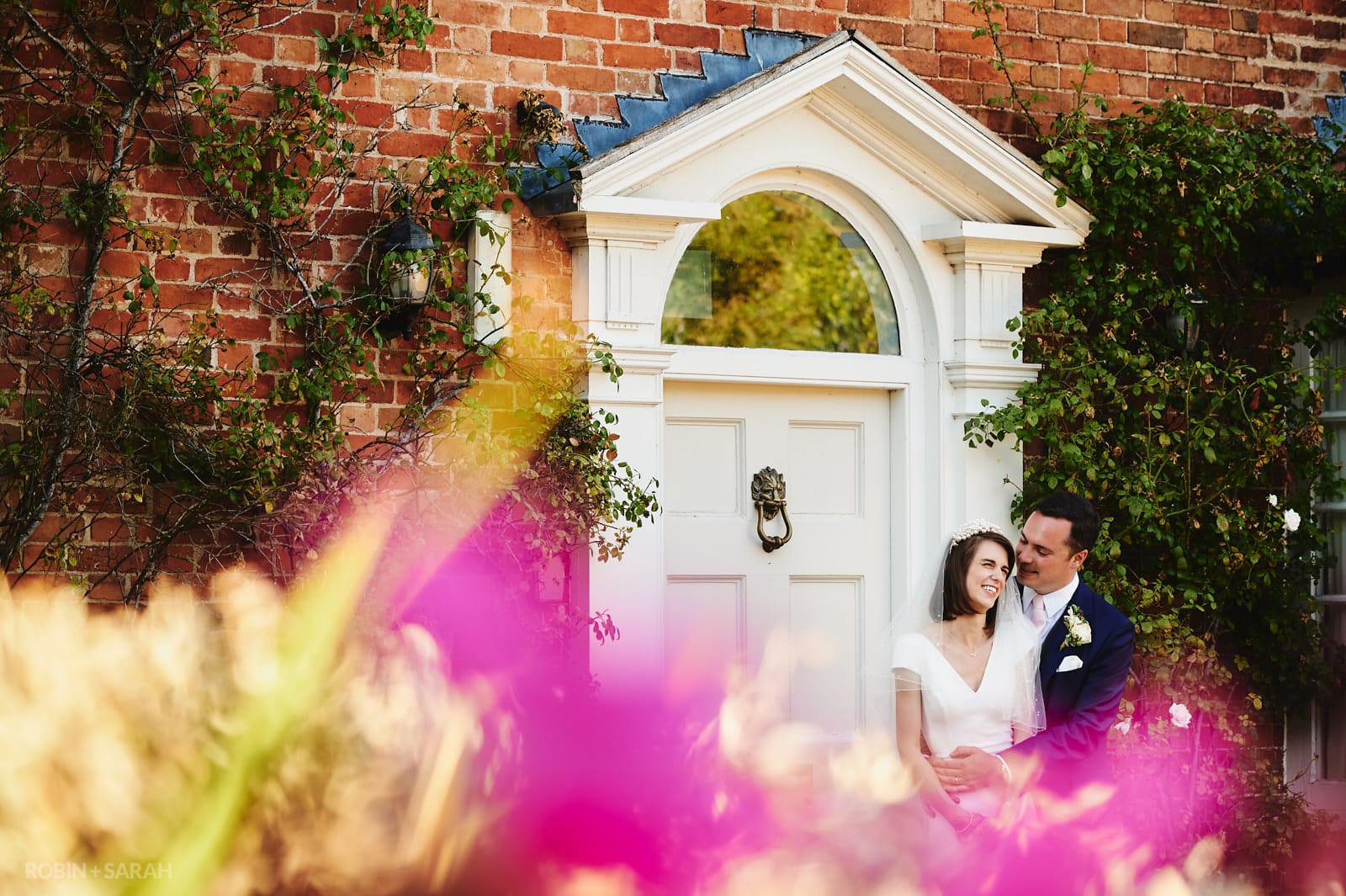 Bride and groom outside main house at Wethele Manor with beautiful coloured flowers in foreground