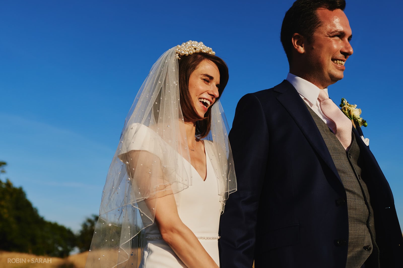 Bride and groom laughing together as they walk through fields