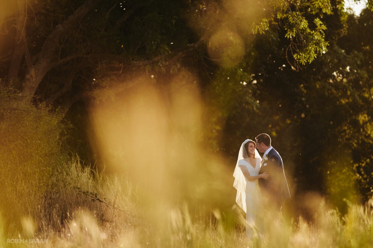 Bride and groom laughing together as they walk through beautiful fields in the evening light