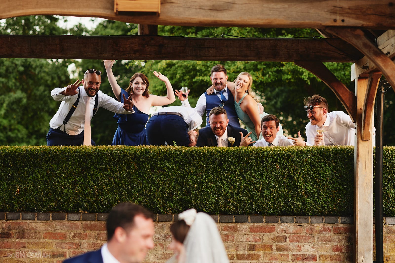 Bride and groom sit on steps as their friends pull faces behind them