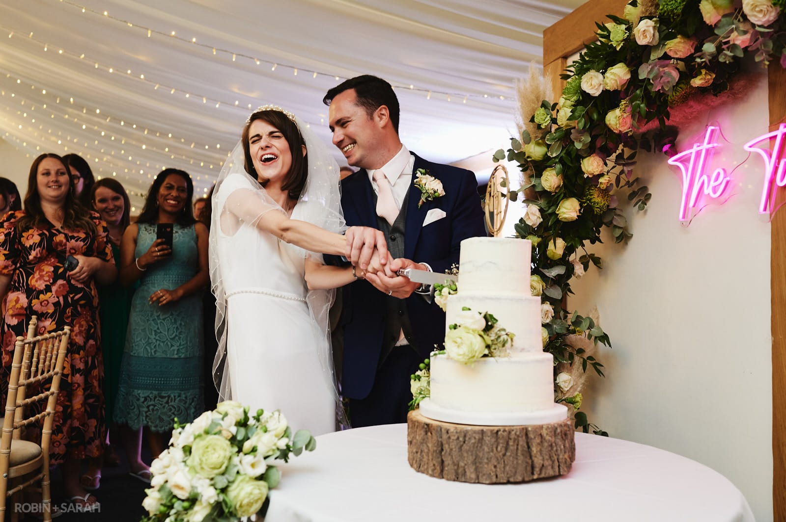 Bride and groom cut wedding cake as guests watch and take photos