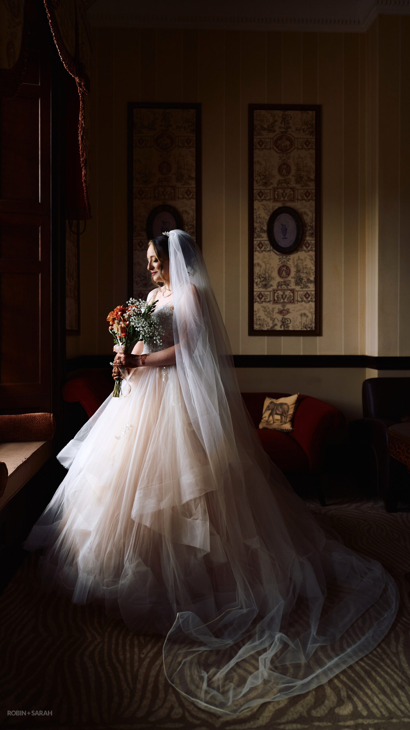Bride with long veil and beautiful wedding dress stands in window light at Spring Grove House