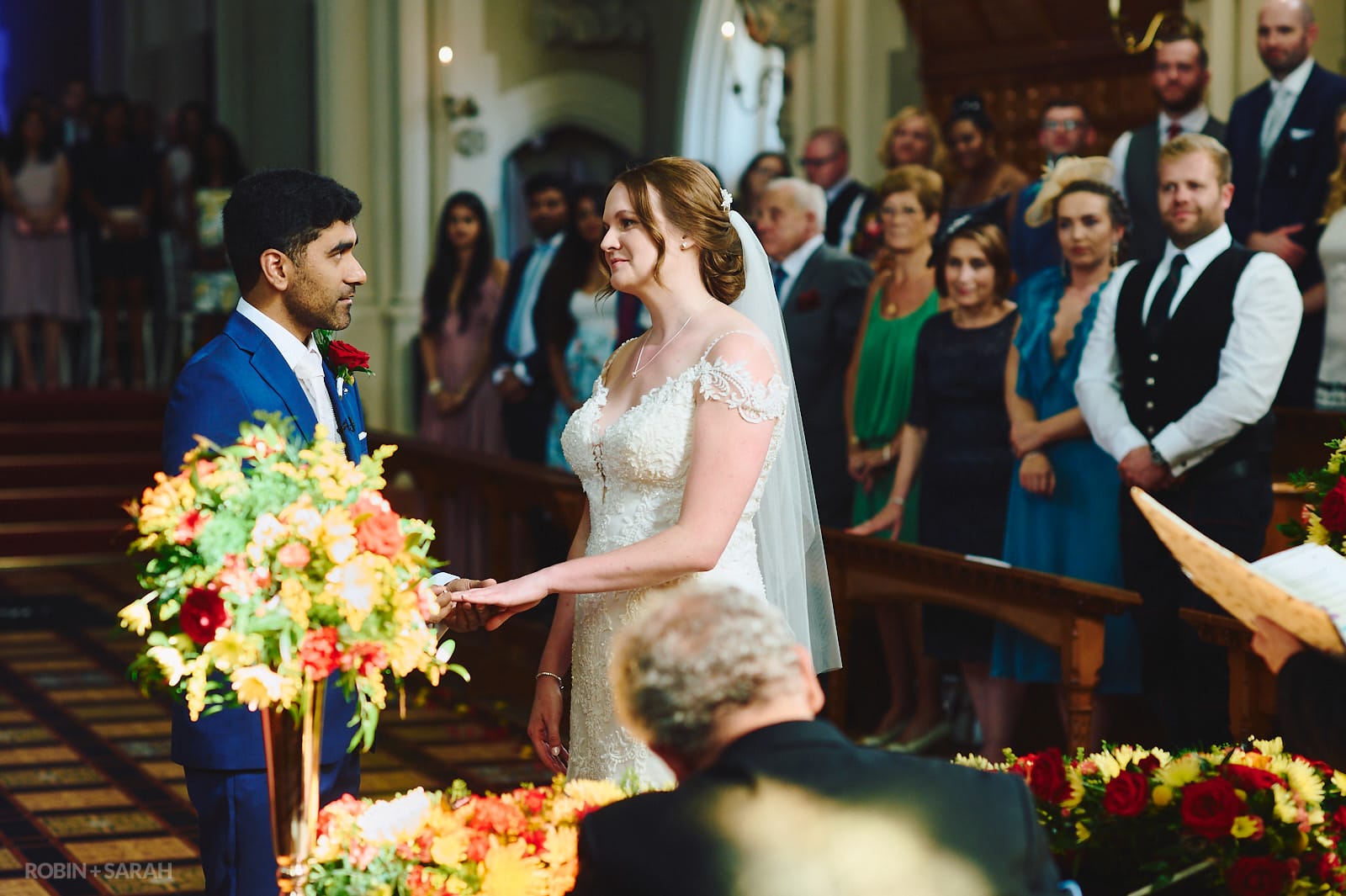Bride and groom exchange wedding rings during ceremony as guests watch