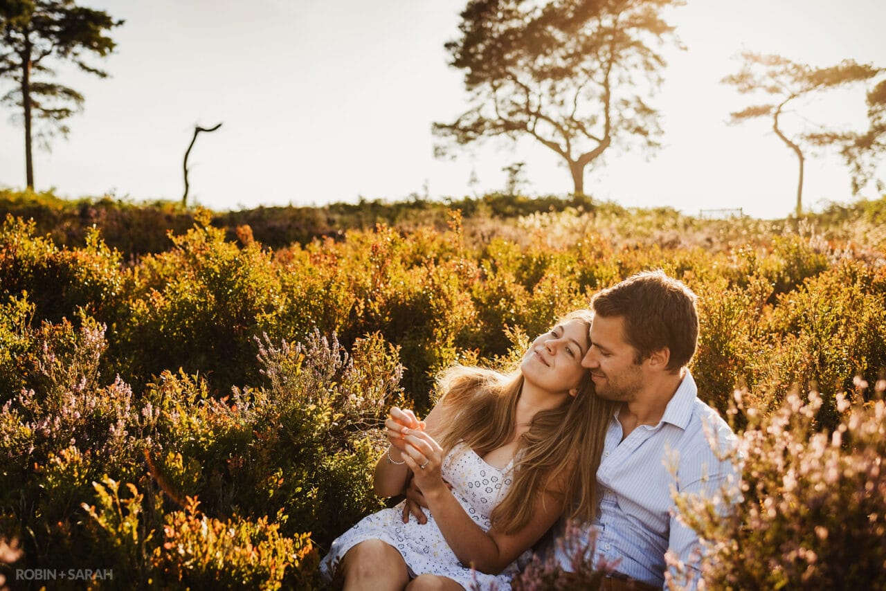 Engaged couple sitting in heather on hilltop location in beautiful light