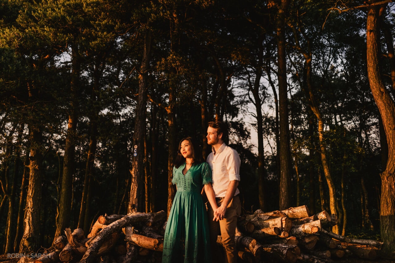 Engaged couple under trees on hilltop location and looking out at the setting sun