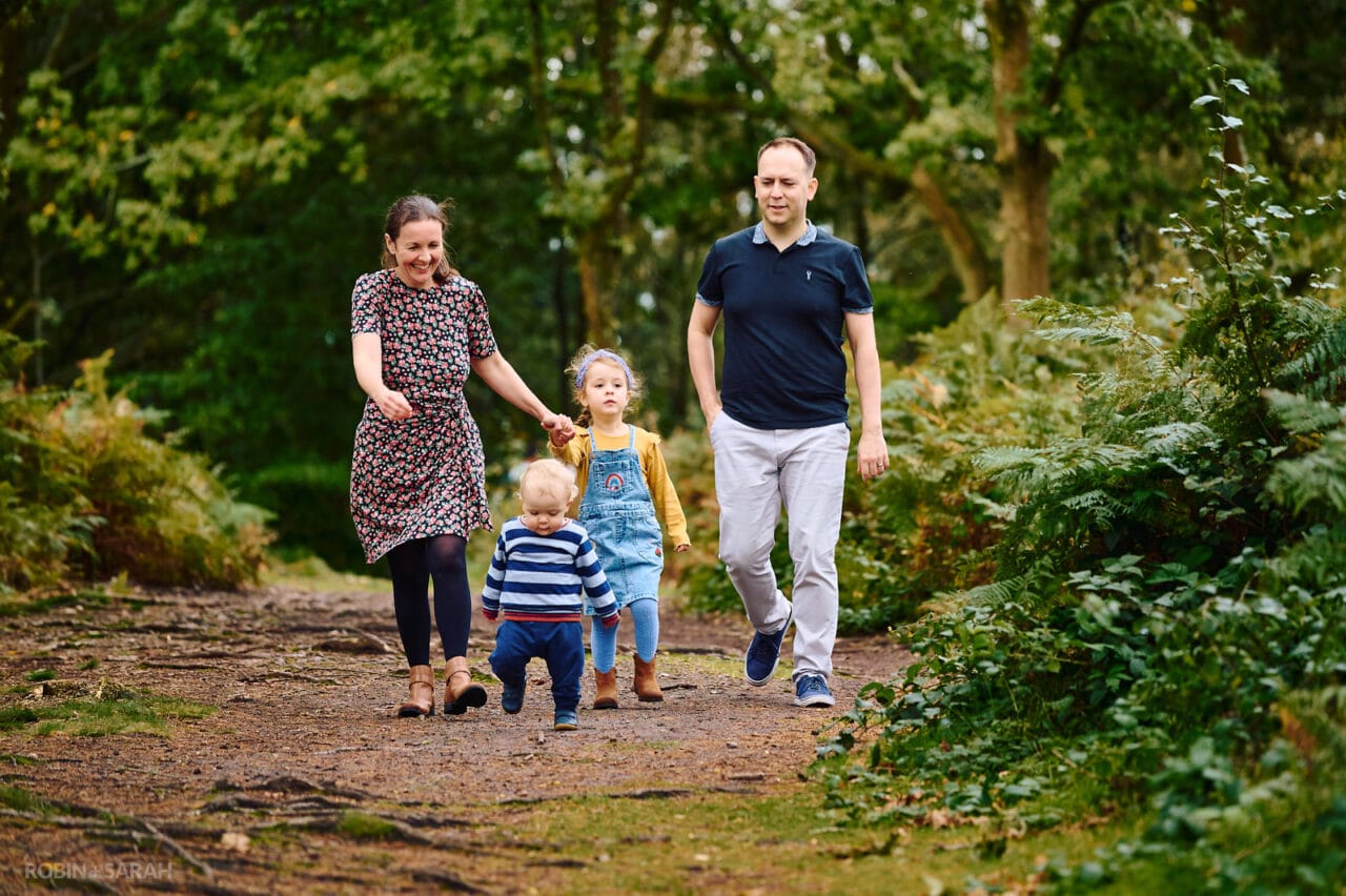 Parents and two kids walk through woods on family photo shoot