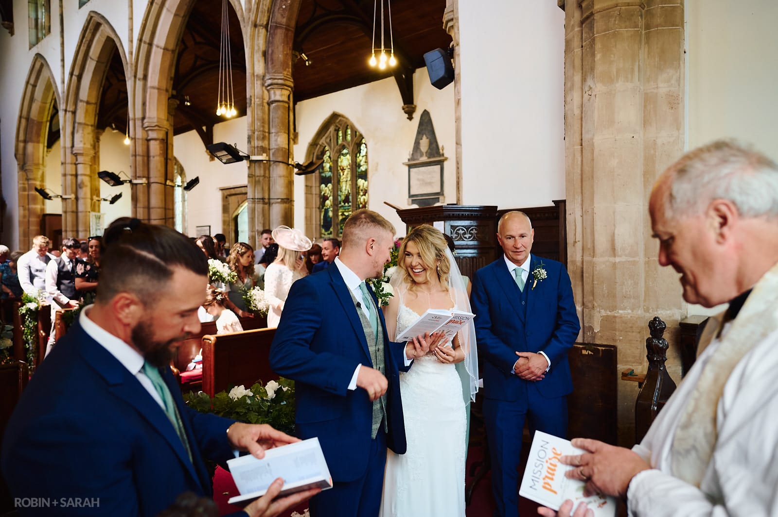 Bride and groom laughing during hymn reading in St Botolph's church Newbold-on-Avon