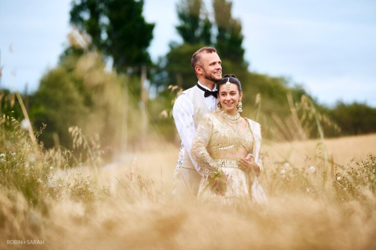 Bride in beautiful Indian wedding dress with her groom as they stand in a crop field