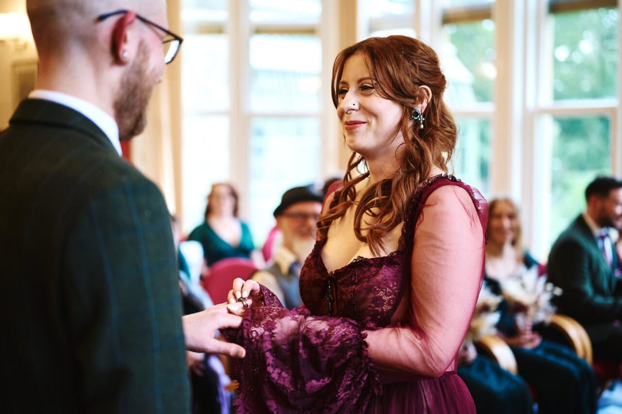 Bride places ring on groom's finger during wedding ceremony in The Elgar Room