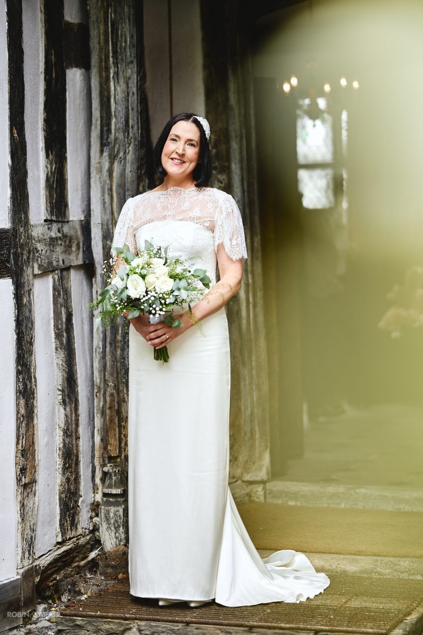 Full-length portrait of bride holding bouquet next to the half-timber walls of Greyfriars in Worcester