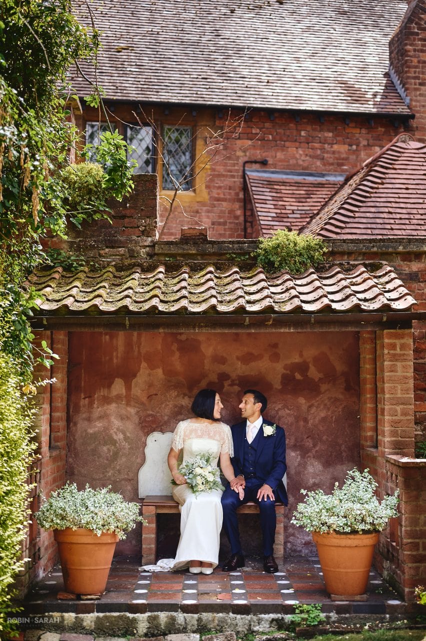 Bride and groom sitting on bench in garden at Greyfriars in Worcester