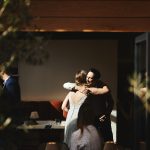 Bride gets hugged by wedding guest in a patch of beautiful sunlight