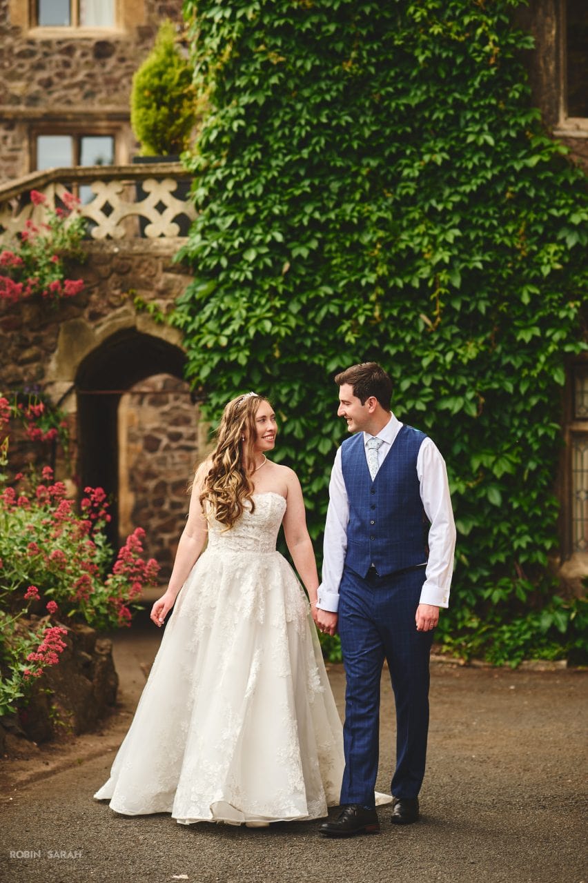 Bride and groom walking through the grounds at the Abbey Hotel, Malvern, with the hotel building in the background