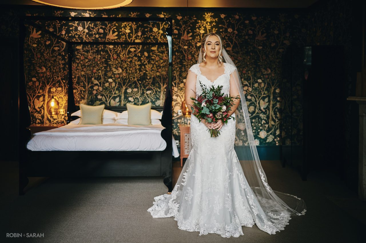 Portrait of bride in wedding dress and veil and holding a bouquet of flowers in one of the bedrooms at Hampton Manor