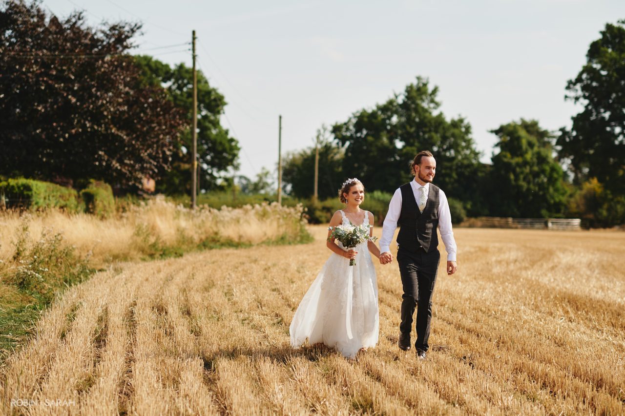 Bride and groom walk through crop fields at Bentley Village Hall near Bromsgrove, Worcestershire