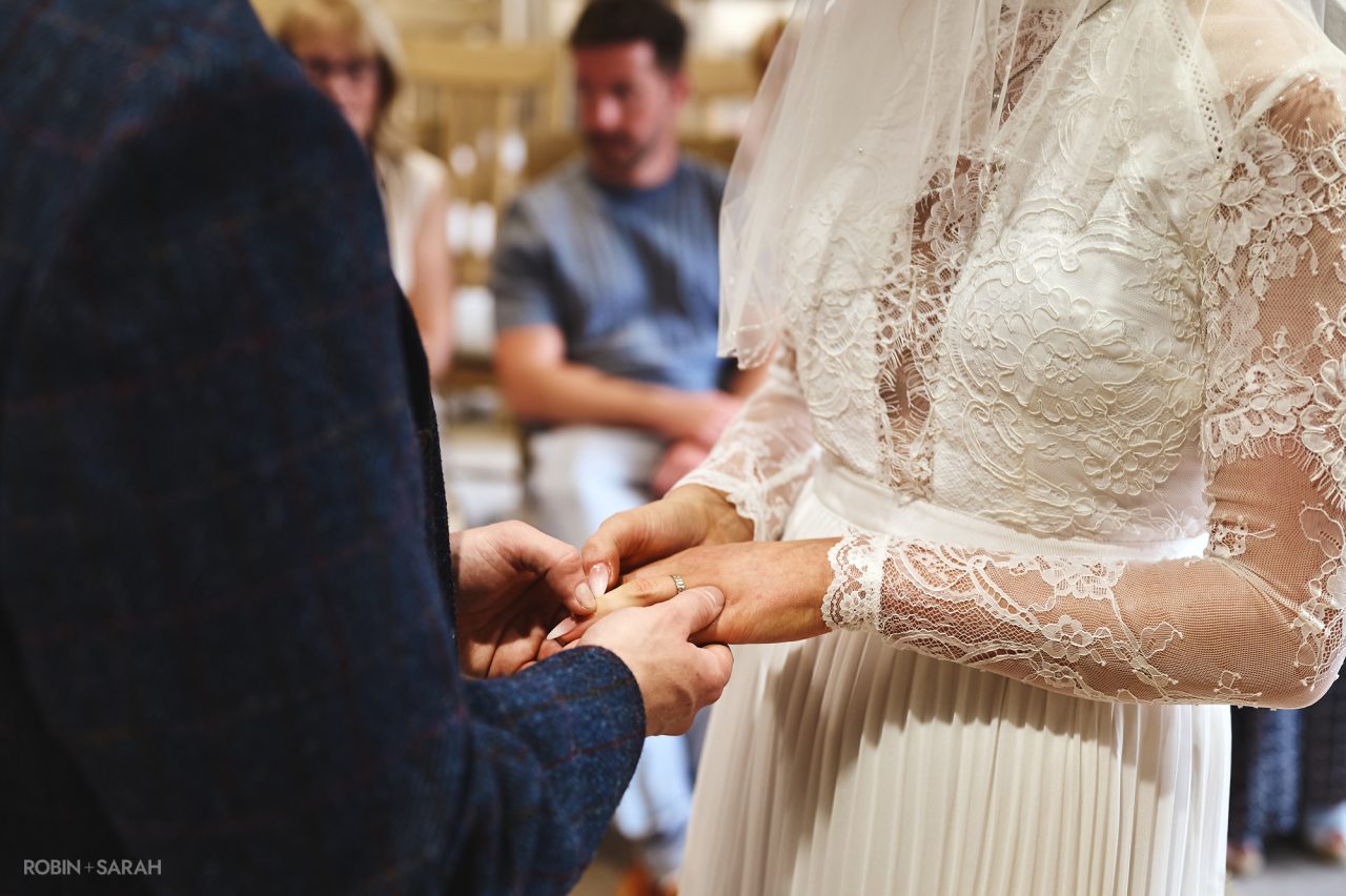 Groom places wedding ring on bride's finger, during a ceremony in The Henley Room