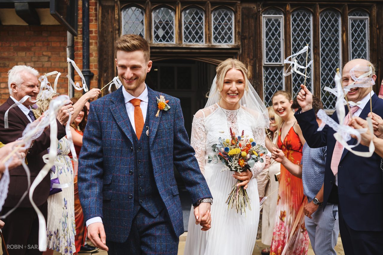 Newly married couple walk out of The Henley Room after their wedding ceremony, as guests wave ribbon wands