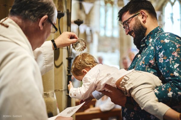 Vicar pours holy water over child's head during baptism at St John the Baptist Church, Brinklow