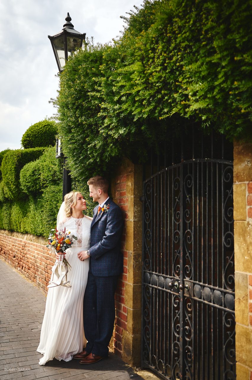 Bride wearing beautiful white wedding dress standing with groom as they lean against an old brick wall in Stratford-upon-Avon