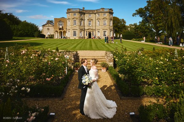 Bride and groom in the rose garden at Bourton Hall in Warwickshire, with the lawn and main house in the background