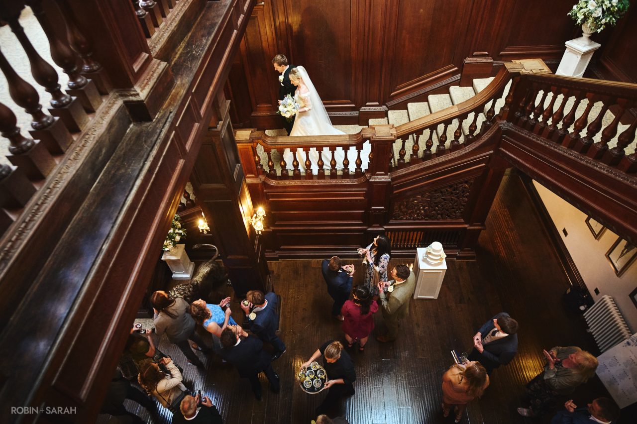 Bride and groom walk down the staircase at Bourton Hall during wedding drinks reception