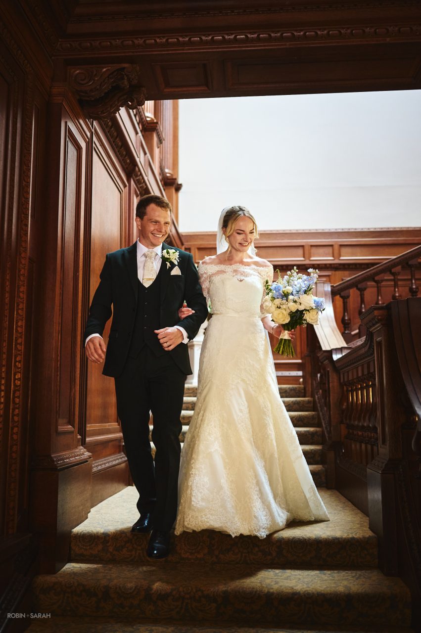 Newly married couple walk down staircase at Bourton Hall to join drinks reception