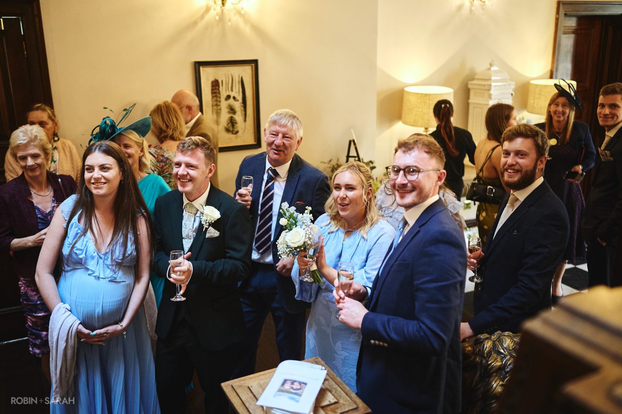 Wedding guests smiling as bride and groom walk down staircase at Bourton Hall in Warwickshire
