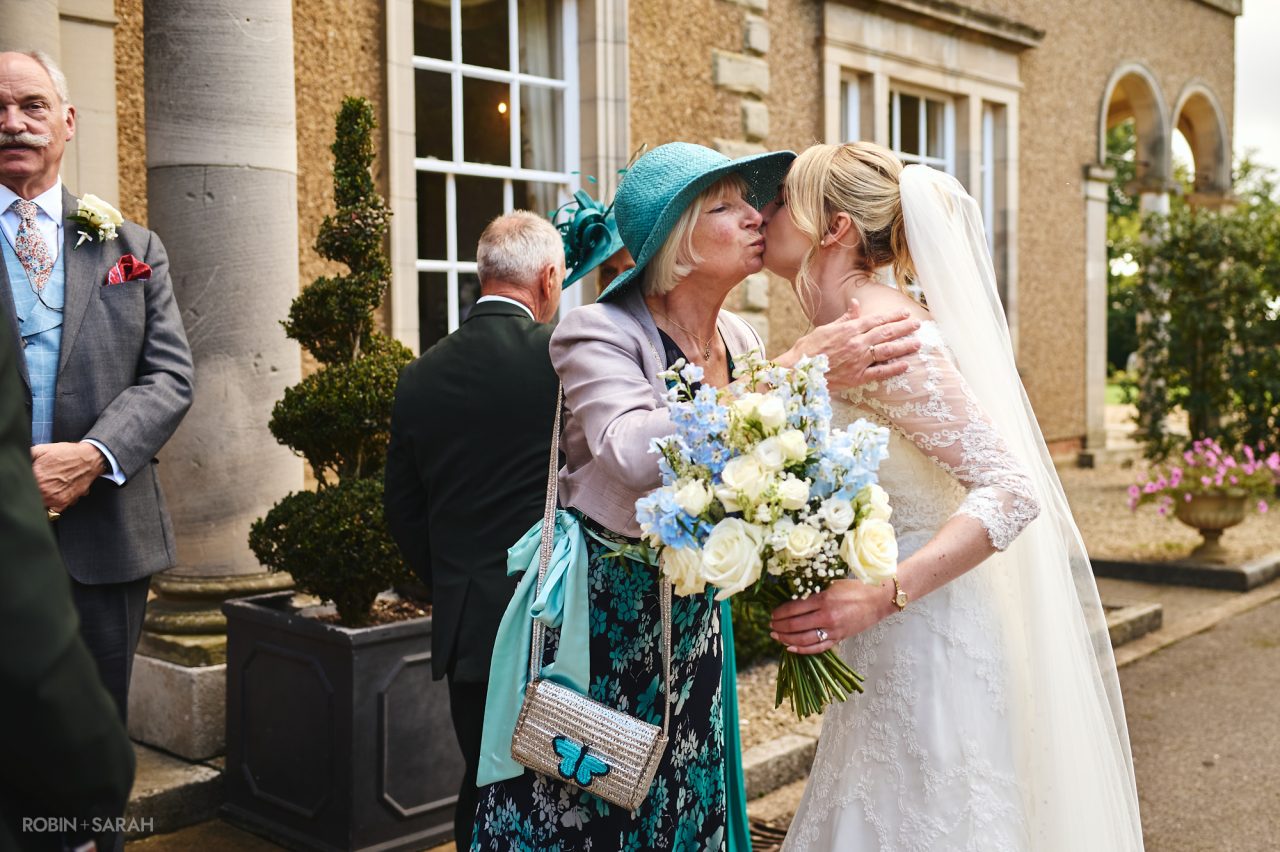 Bride receives kiss from mum outside Bourton Hall in Warwickshire