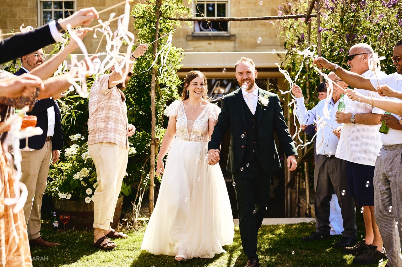 Bride and groom walking through guests as they wave ribbon wands and blow bubbles