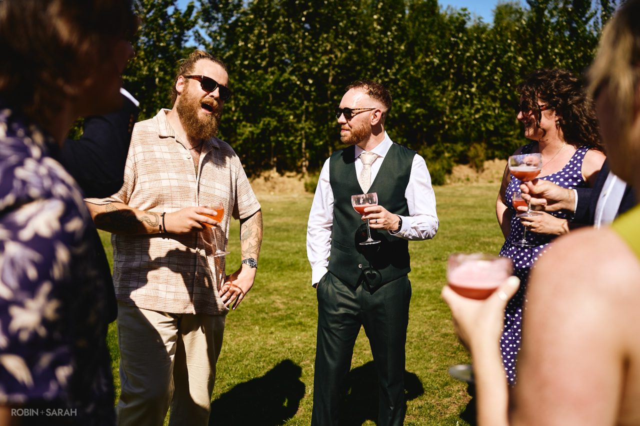 Groom chats with wedding guests as they all enjoy a drink in the gardens at Charingworth House