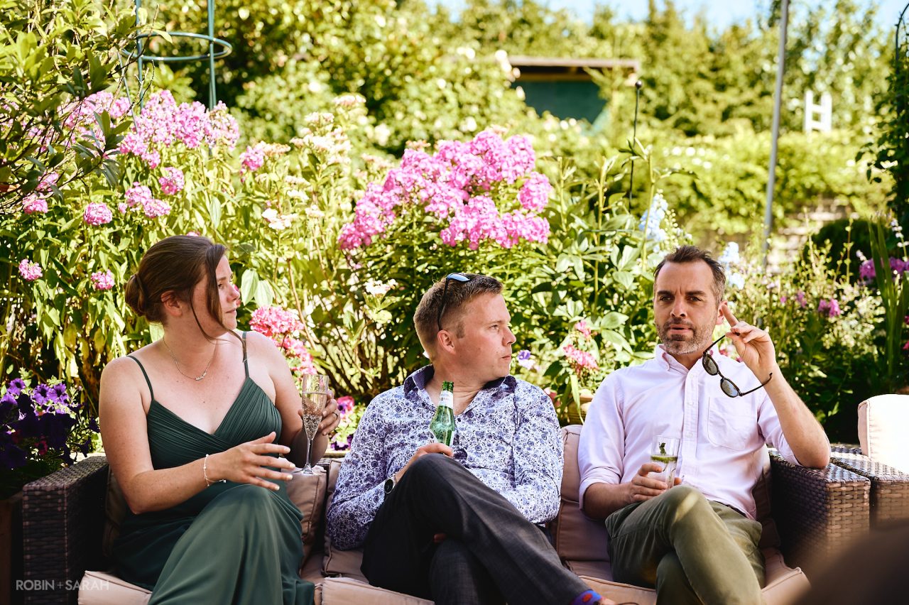 Wedding guests relax and chat with drinks in beautiful gardens on a sunny day