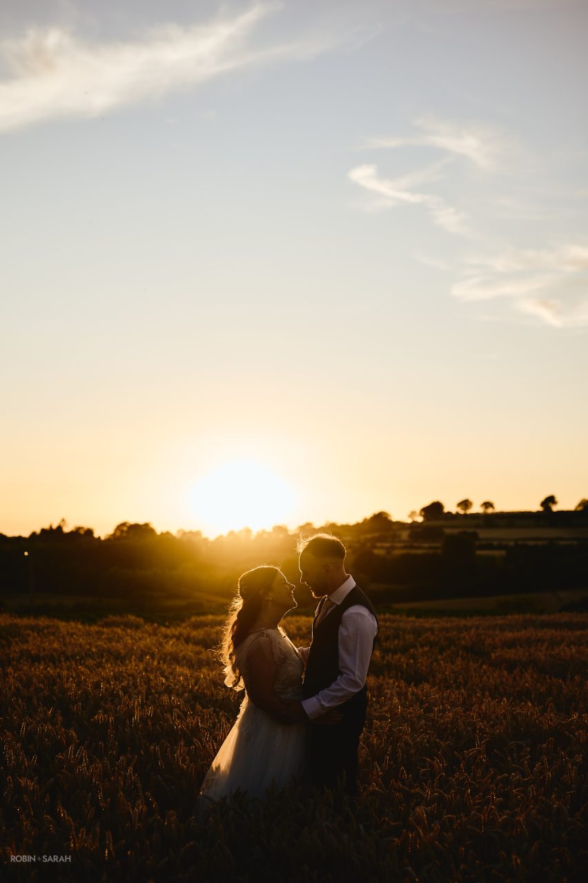 Bride, groom and setting sun in crop fields at Charingworth House